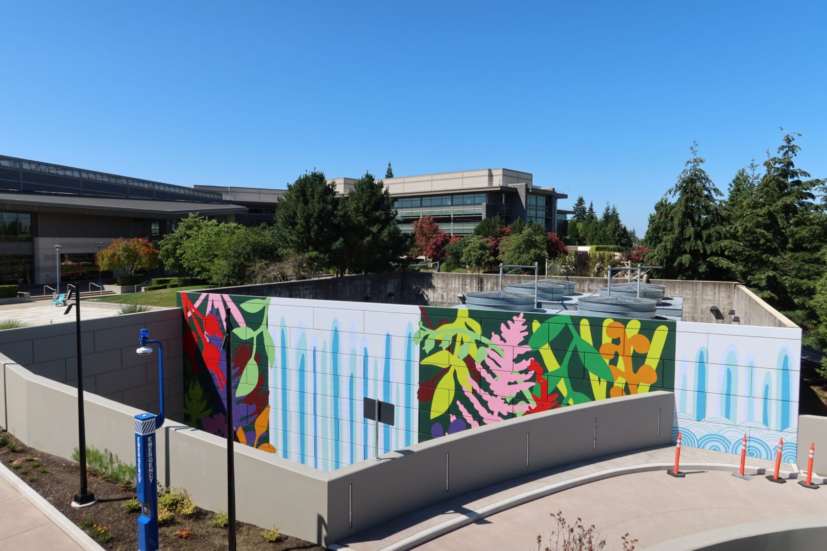 an overhead view of a massive, colorful mural on the wall of a parking garage. The scale of the mural can be seen by the view of buildings and trees in the background.