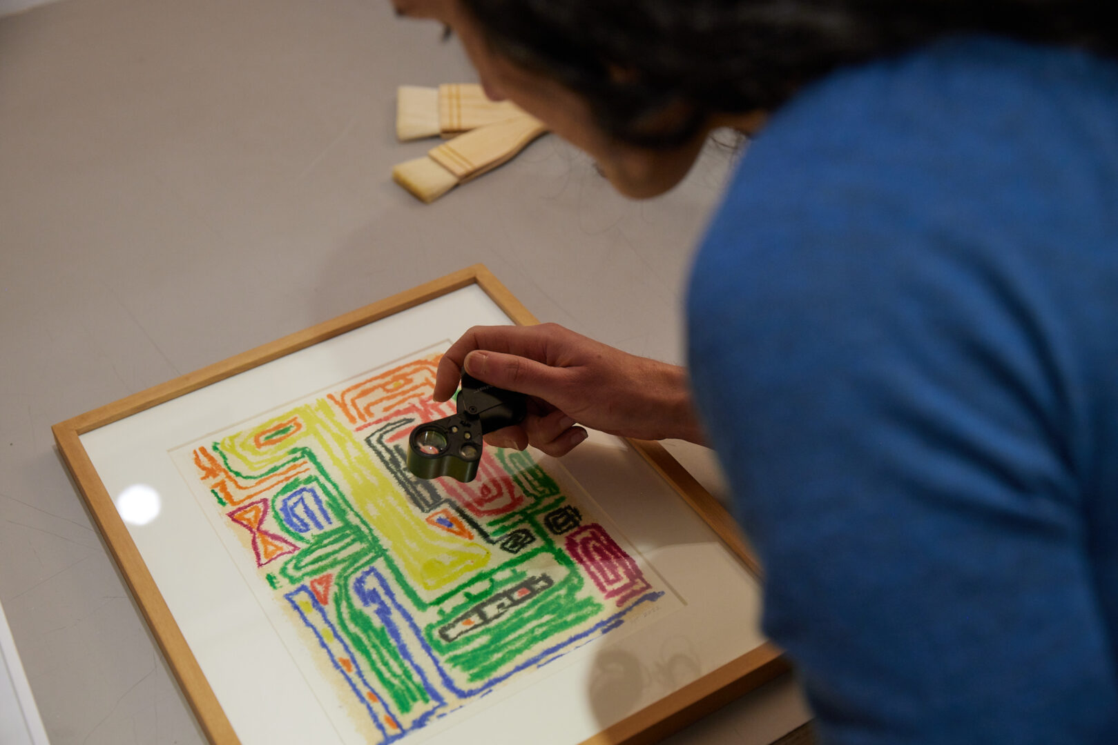 someone peers through a magnifying loupe at an artwork