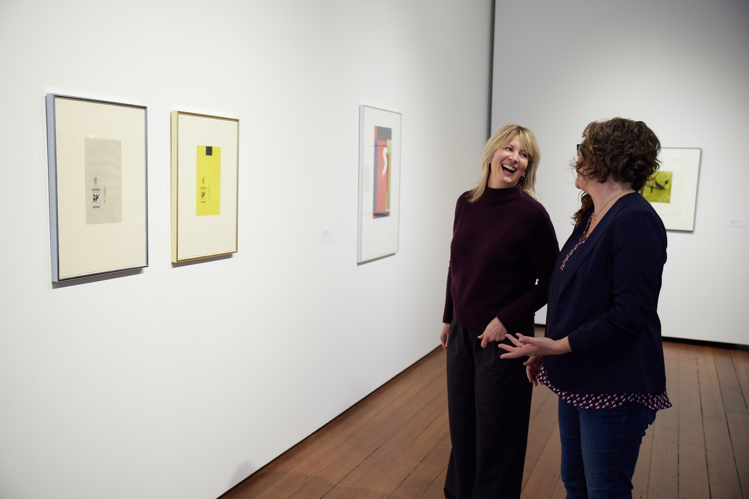 Two women chat and laugh in an art gallery