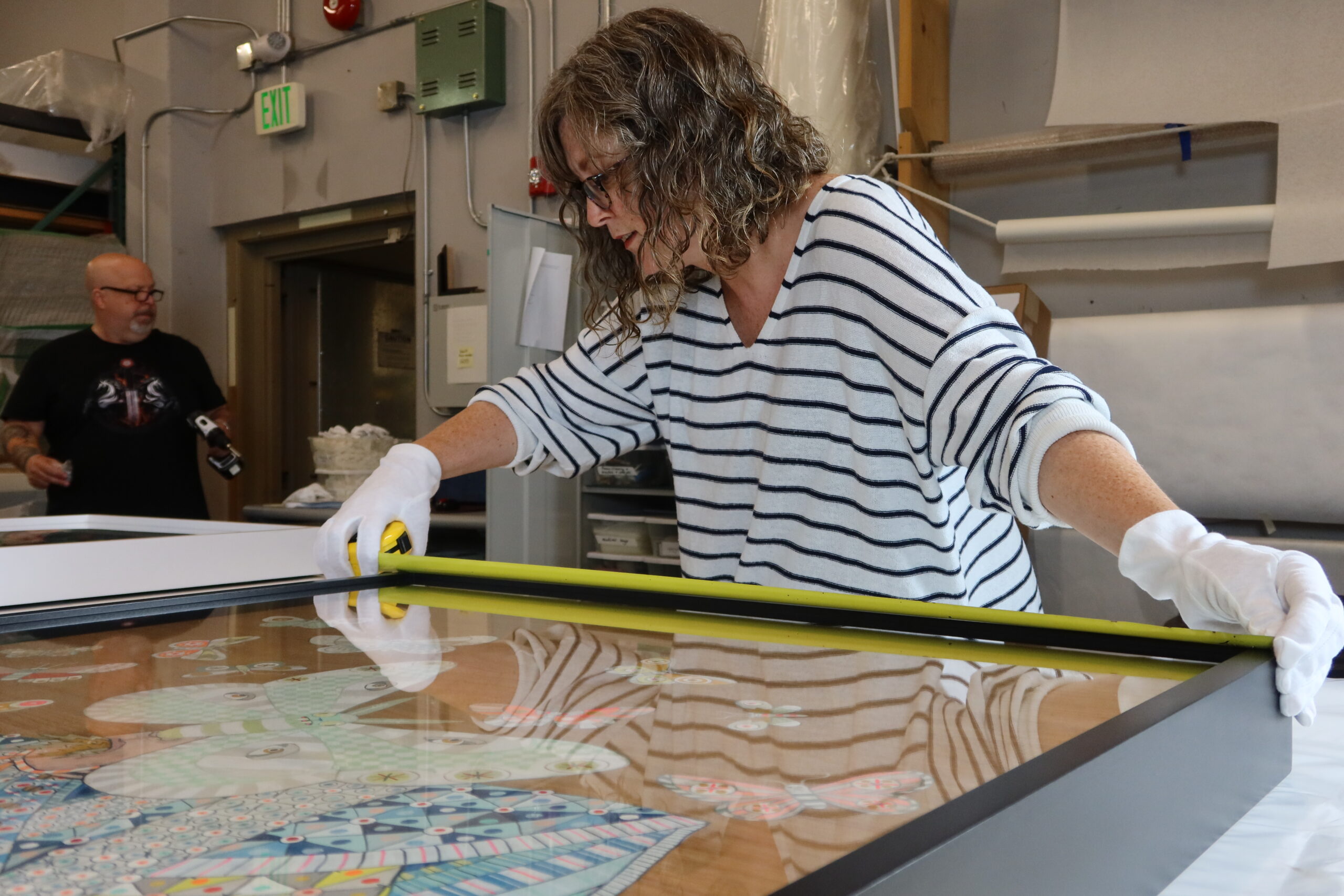 A woman wearing white gloves measures a framed artwork