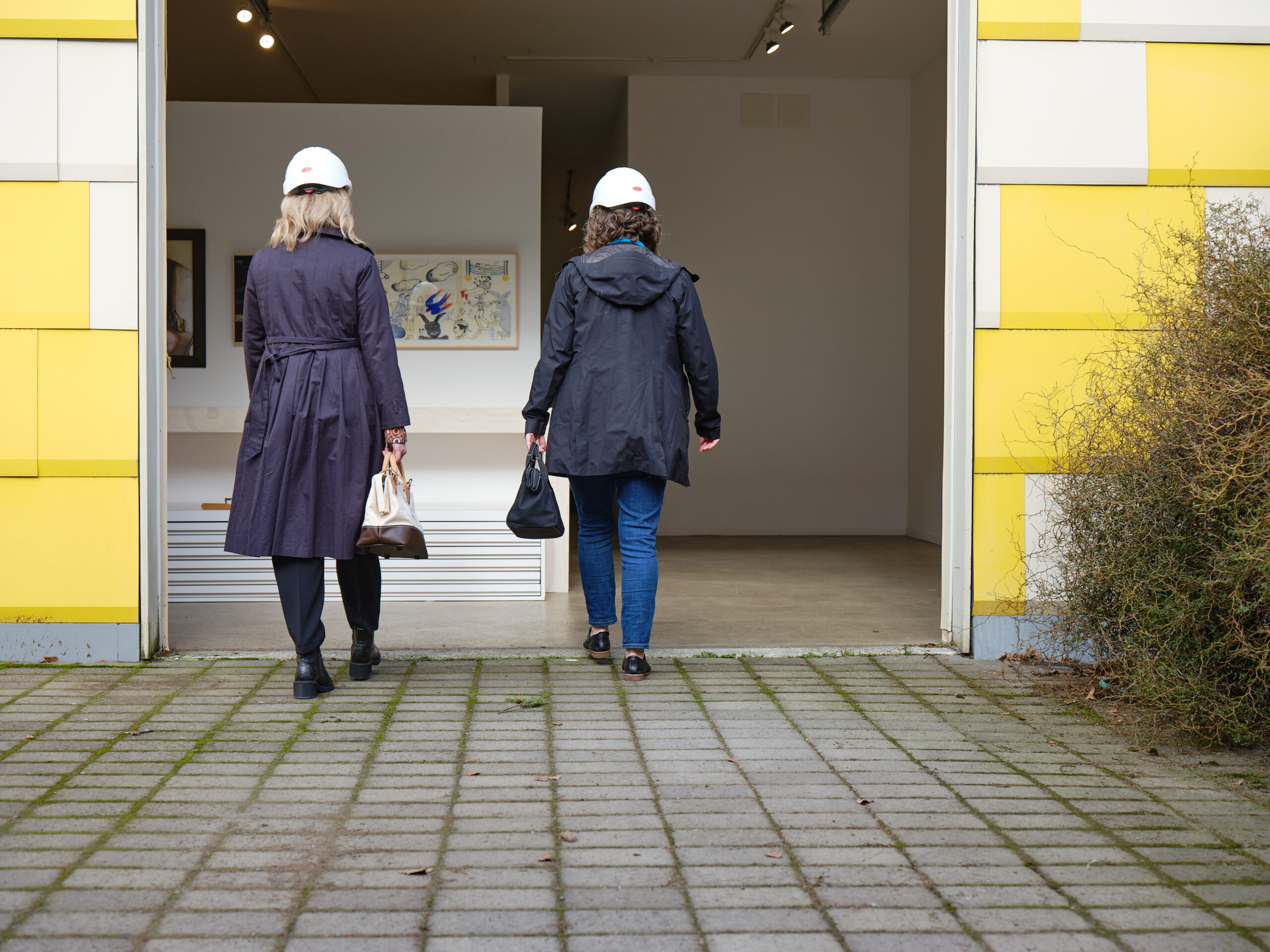 Two women in hardhats walk into an art gallery