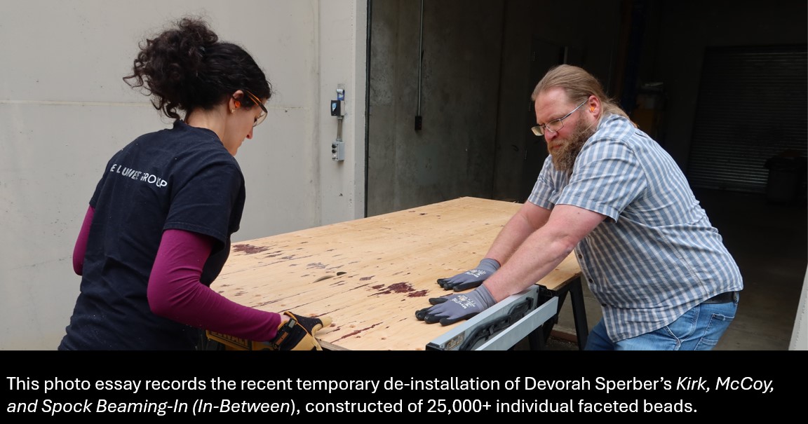 Two art professionals cut plywood on a table saw, with text beneath that reads, "This photo essay records the recent temporary de-installation of Devorah Sperber's "kirk, McCoy, and Spock Beaming-In (In-Between)," constructed of 25,000 individual faceted beads.